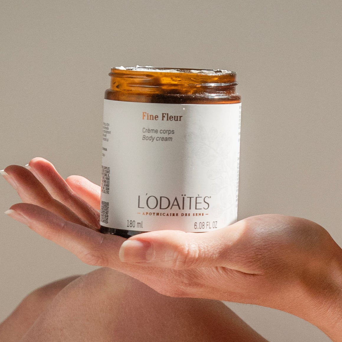 Pot ouvert de crème corps Fine Fleur de L'Odaïtès posé sur une main de femme