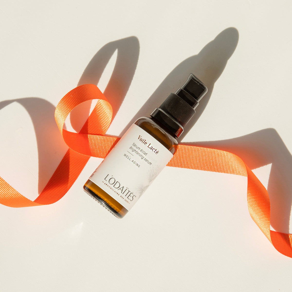 Sérum éclat Voile Lacté de L'Odaïtès avec un ruban orange et une lumière chaude