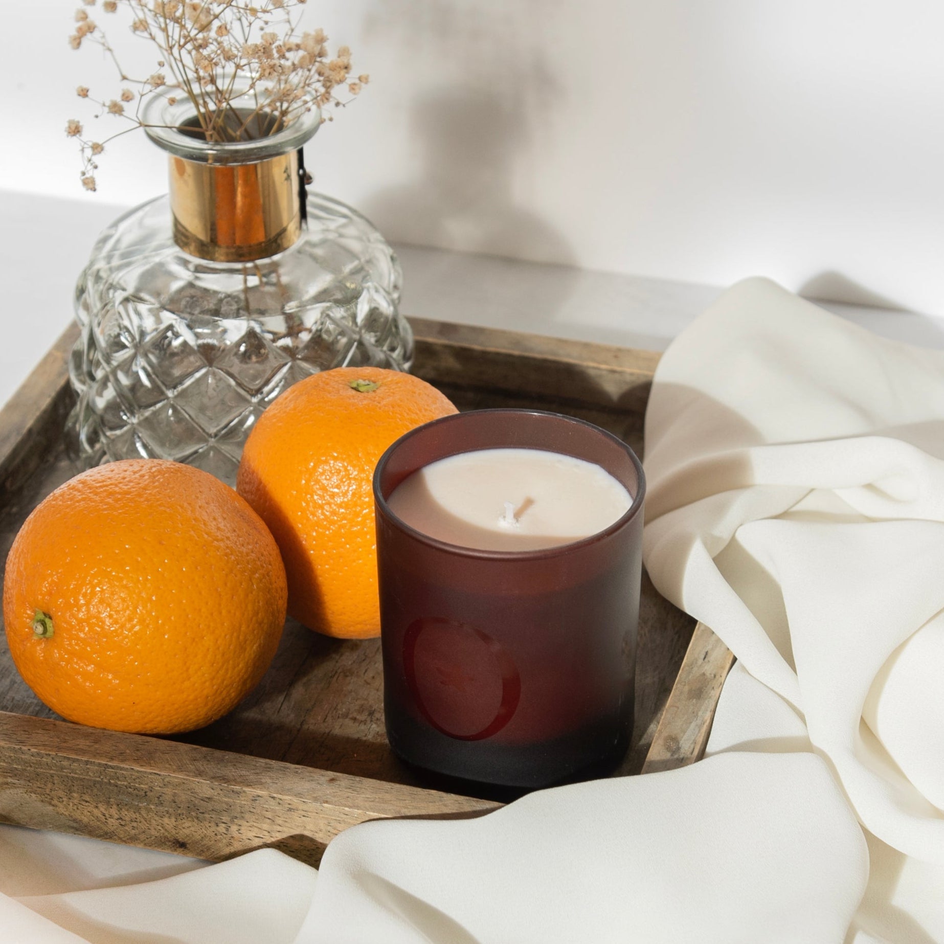 Bougie parfumée Orangeraie en Fleur de L'Odaïtès posée sur un plateau en bois avec deux oranges et un vase
