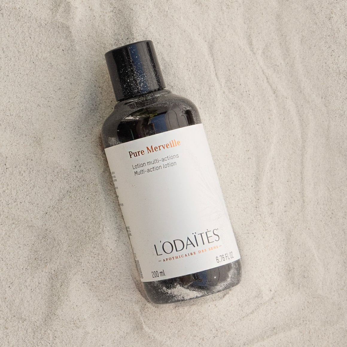 Lotion multi-actions Pure Merveille de L'Odaïtès posée sur du sable
